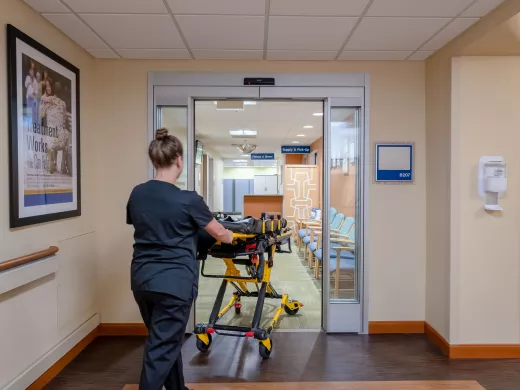 A healthcare worker wheeling a gurney through a set of doors.