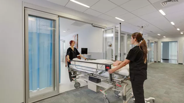 A hospital bed wheeled out of a set of doors.