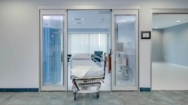 A hospital bed being wheeled out of a set of doors.