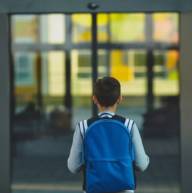 student-door.jpg young boy in backpack standing in front of doors