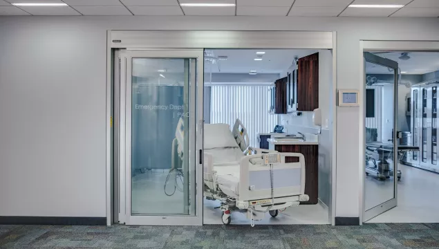 A set of sliding doors in a hospital room with a bed coming through the doors.