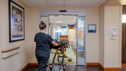 A healthcare worker wheeling a gurney through a set of doors.